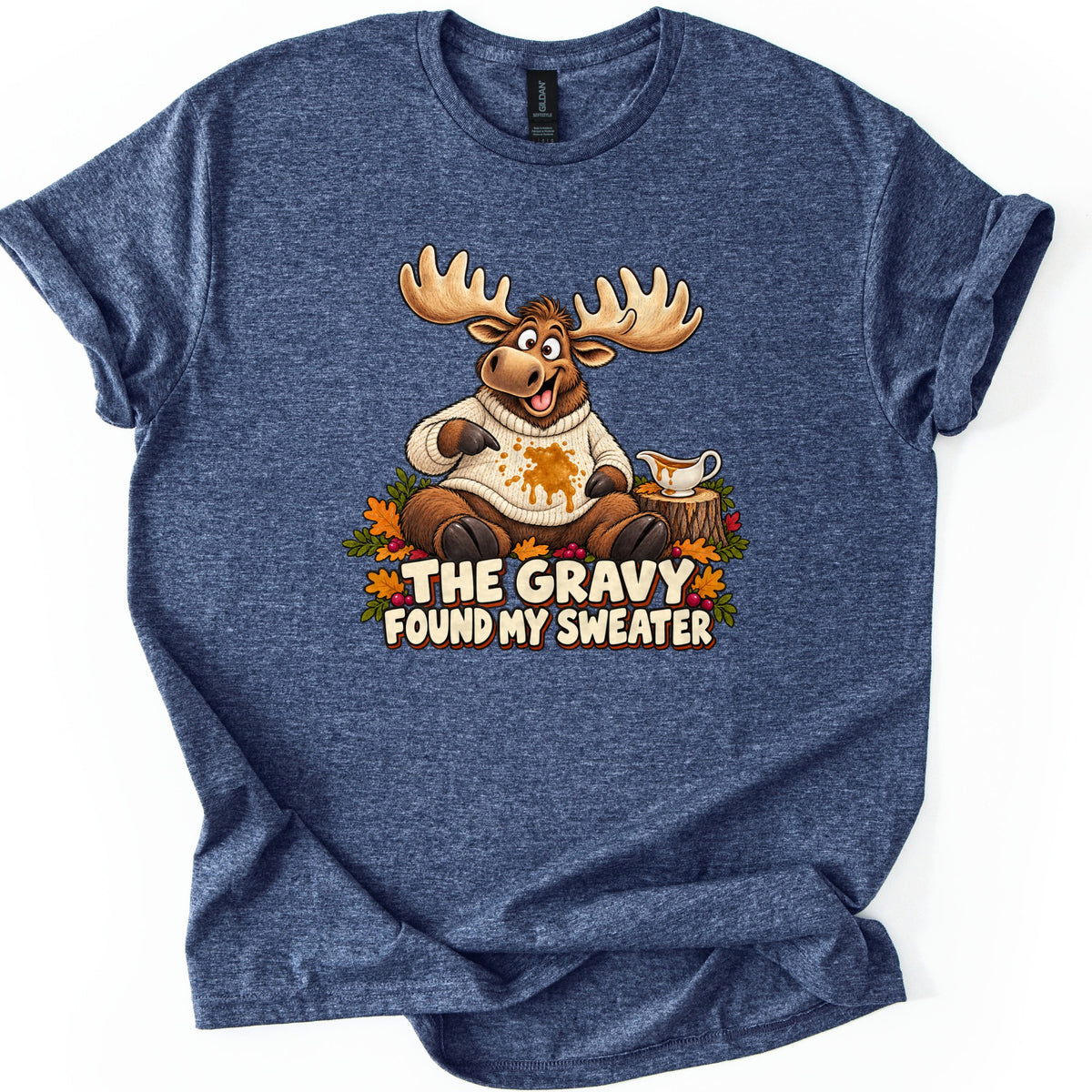 The Gravy Found My Sweater Comfort Colors T-shirt in Heather Navy, laid flat. A cartoon moose sits among fall leaves and berries pointing at gravy spilled on his cream knit sweater, a gravy boat on a stump beside him, above the words The Gravy Found My Sweater. Shown on a white background.