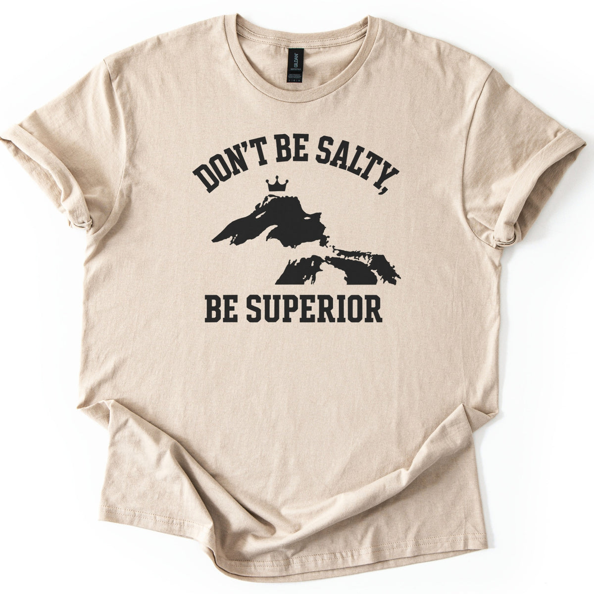 Be Superior Comfort Colors T-shirt in Sand, laid flat. A black print shows the words Don't Be Salty, arched over a silhouette of the Great Lakes with a small crown above Lake Superior, and Be Superior below. Sleeves are cuffed on a white background.