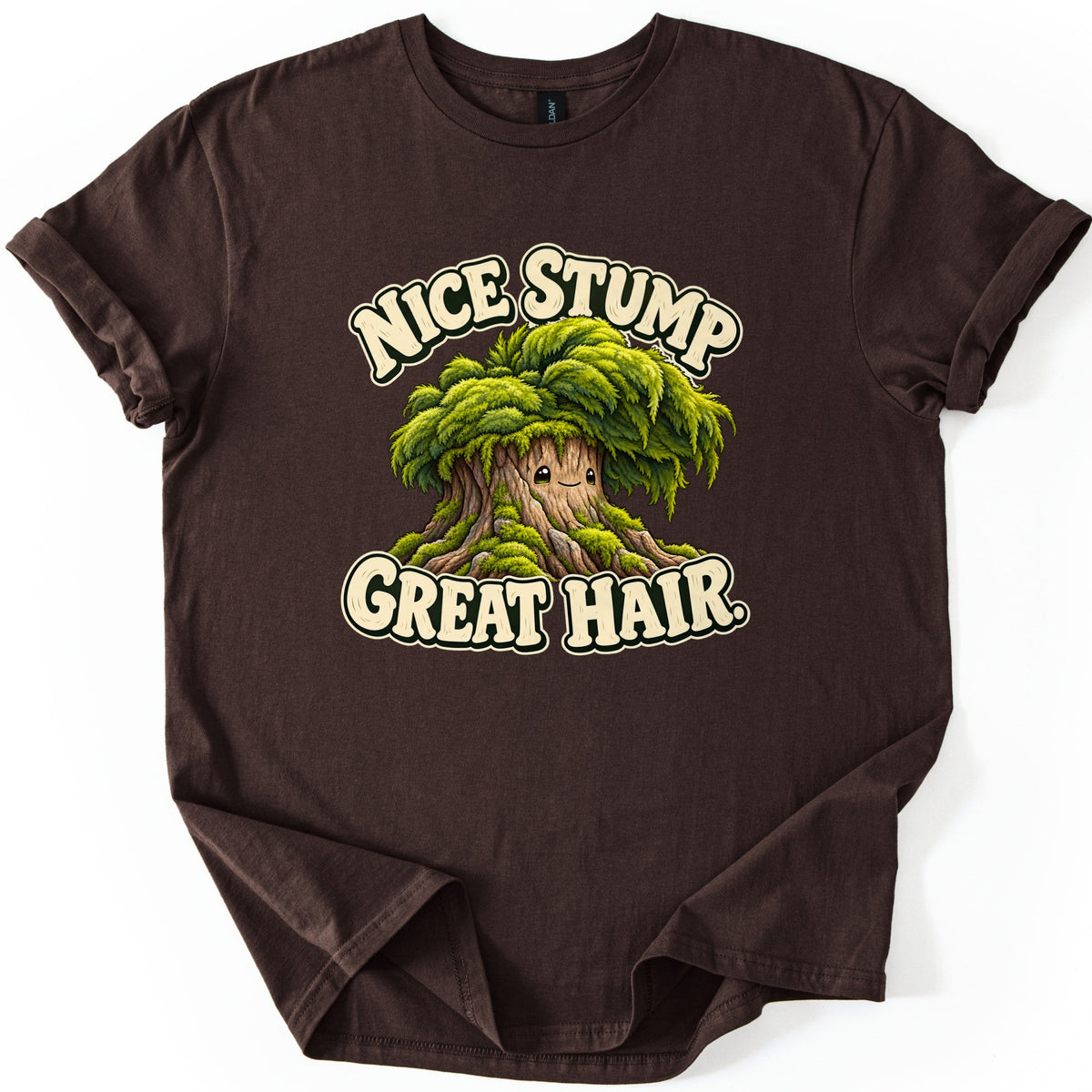Nice Stump Great Hair Comfort Colors T-shirt in Dark Chocolate, laid flat. A smiling cartoon tree stump with a thick mop of green moss like hair, between the words Nice Stump and Great Hair. in cream letters. The shirt has rolled sleeves and lies on a white background.