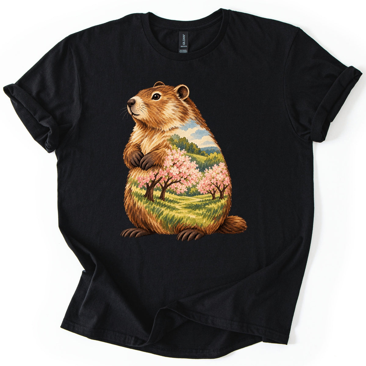 Groundhog Blossom Meadow Comfort Colors T-shirt in Black, laid flat. A painted groundhog sits upright with paws at its chest, its body filled with a meadow of pink blossoming trees, green hills and blue sky. No words. Sleeves cuffed, on a white background.