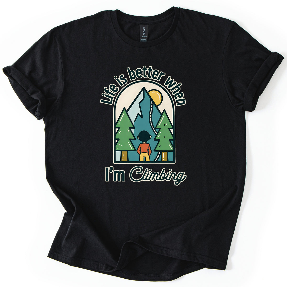 Better When I'm Climbing Comfort Colors T-shirt in Black, laid flat. The words Life is better when arch over a window scene of a person facing a teal mountain with a winding trail, a yellow sun and two pine trees, with I'm Climbing below. Sleeves rolled, on a white surface.