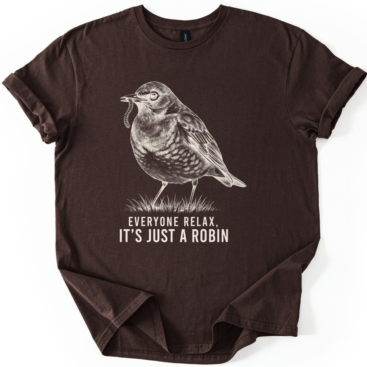 Everyone Relax It's Just A Robin Comfort Colors T-shirt in Dark Chocolate, laid flat. A cream sketch-style drawing of a robin holding a worm in its beak, standing on a tuft of grass, above the words Everyone Relax, It's Just A Robin. The sleeves are rolled on a white background.