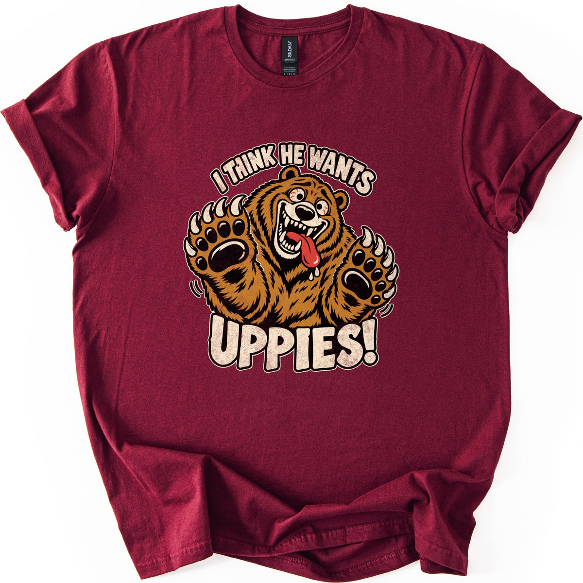 I Think He Wants Uppies Comfort Colors T-shirt in Maroon, laid flat. A wild-eyed cartoon brown bear with a drooling tongue reaches up with both clawed paws between the words I Think He Wants and Uppies! The sleeves are cuffed on a white background.