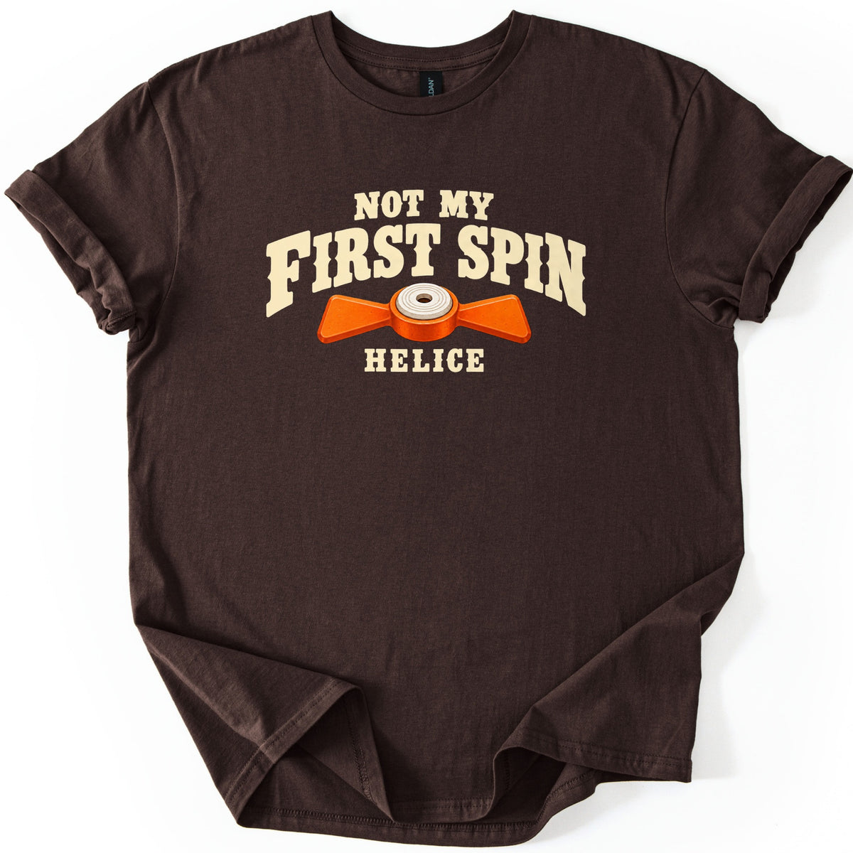 Not My First Spin Comfort Colors T-shirt in Dark Chocolate, laid flat. Cream western-style letters read Not My First Spin above an orange two-bladed propeller target with a white center, with the word Helice below. The shirt lies on a white surface with sleeves cuffed.