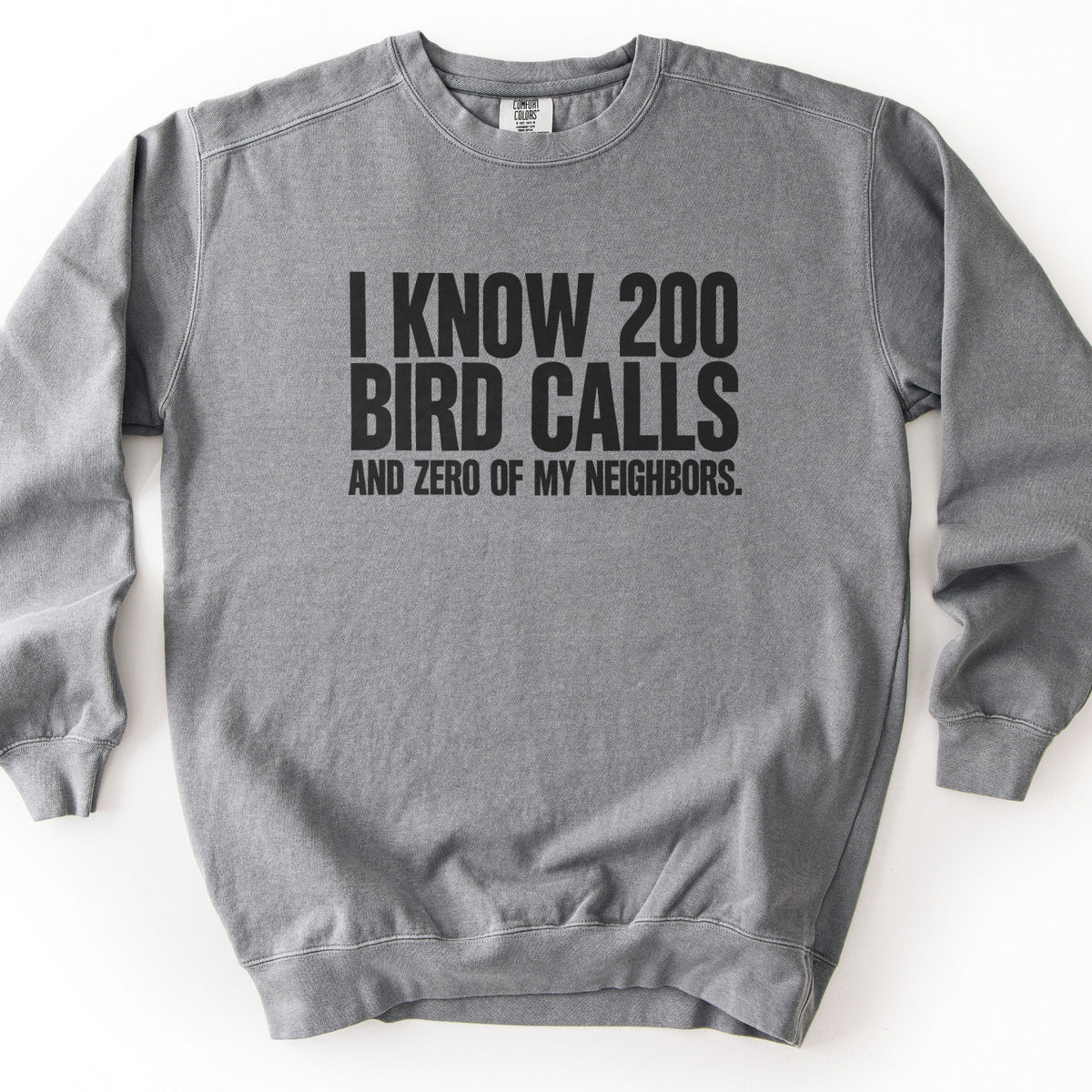 I Know 200 Bird Calls and Zero of My Neighbors Comfort Colors crewneck sweatshirt in Grey, laid flat. Bold black capital letters across the chest read I Know 200 Bird Calls, with And Zero of My Neighbors. in smaller letters below. The sweatshirt lies on a plain white background.