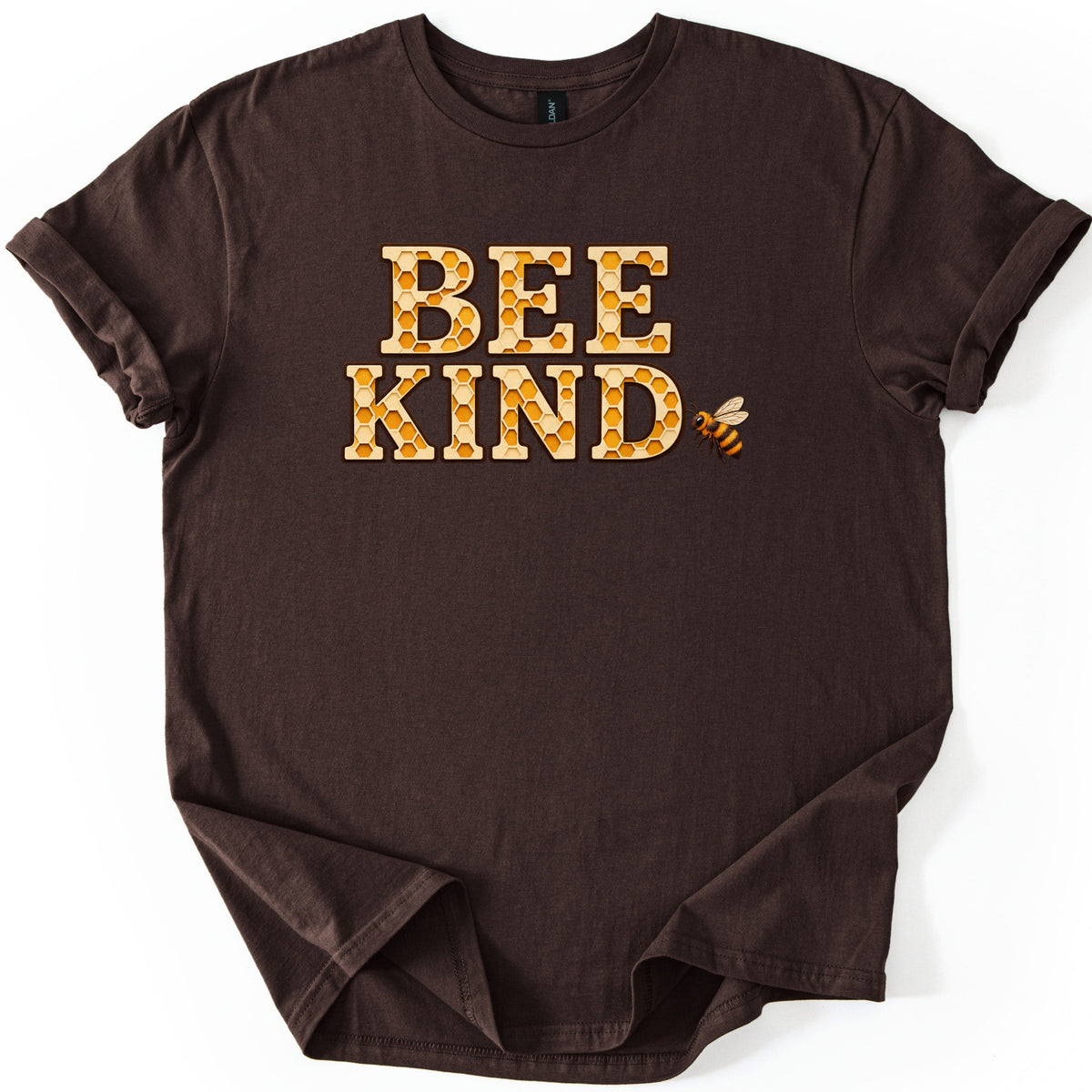Bee Kind Comfort Colors T-shirt in Dark Chocolate, laid flat. The words BEE KIND in large block letters filled with golden honeycomb, outlined in brown, with a small striped honeybee beside the D. The shirt has rolled sleeves and lies on a white background.
