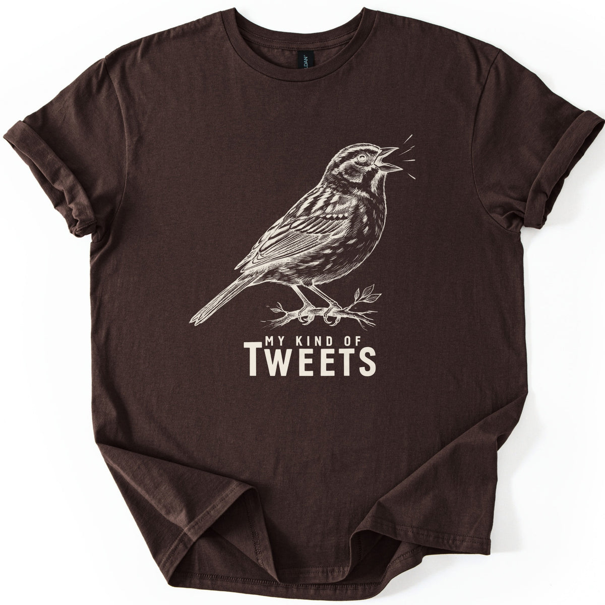 My Kind Of Tweets Comfort Colors T-shirt in Dark Chocolate, laid flat. A cream sketch-style drawing of a sparrow singing on a leafy twig, with short lines by its open beak, above the words My Kind Of Tweets in cream. The sleeves are cuffed and the shirt fills the frame.