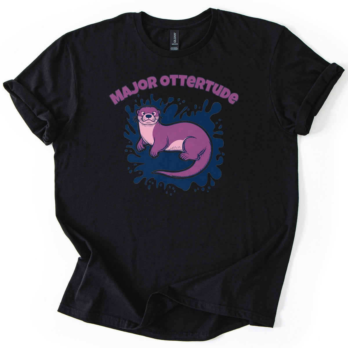 Major Ottertude Comfort Colors T-shirt in Black, laid flat. Arched purple letters reading MAJOR OTTERTUDE top a purple cartoon otter with a pink chest lying on a navy blue paint splash. The shirt has cuffed sleeves and lies on a white background.