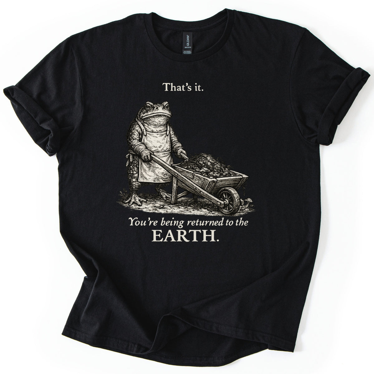 Toad Compost Comfort Colors T-shirt in Black, laid flat. A cream ink etching of a frowning toad in an apron pushing a wheelbarrow of compost, between the words That's it. and You're being returned to the EARTH. Sleeves are cuffed on a white background.