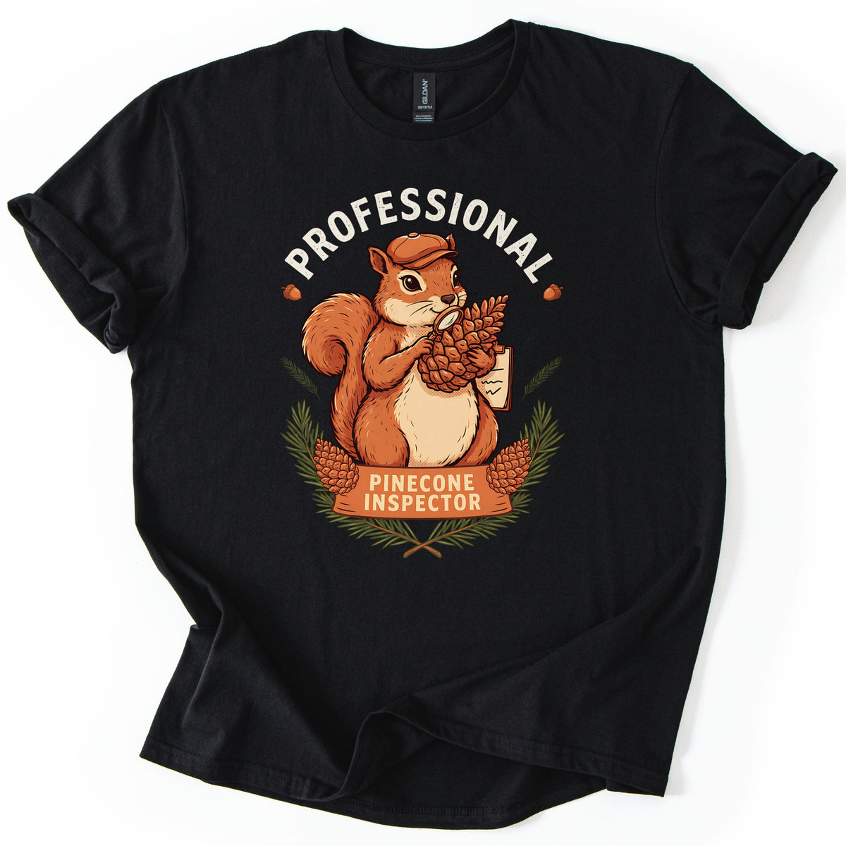 Professional Pinecone Inspector Comfort Colors T-shirt in Black, laid flat. A squirrel in a cap inspects a pinecone with a magnifying glass under the arched word Professional in white, above a banner reading Pinecone Inspector framed by pine branches. Sleeves are cuffed on a white surface.