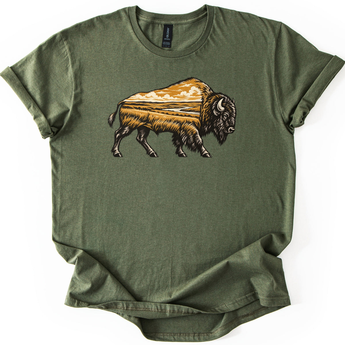 Prairie Bison Comfort Colors T-shirt in Military Green, laid flat. A woodcut-style bison walks in side profile, its body filled with a golden prairie scene of tall grass, a winding river and clouds. No words. The shirt has cuffed sleeves on a white background.