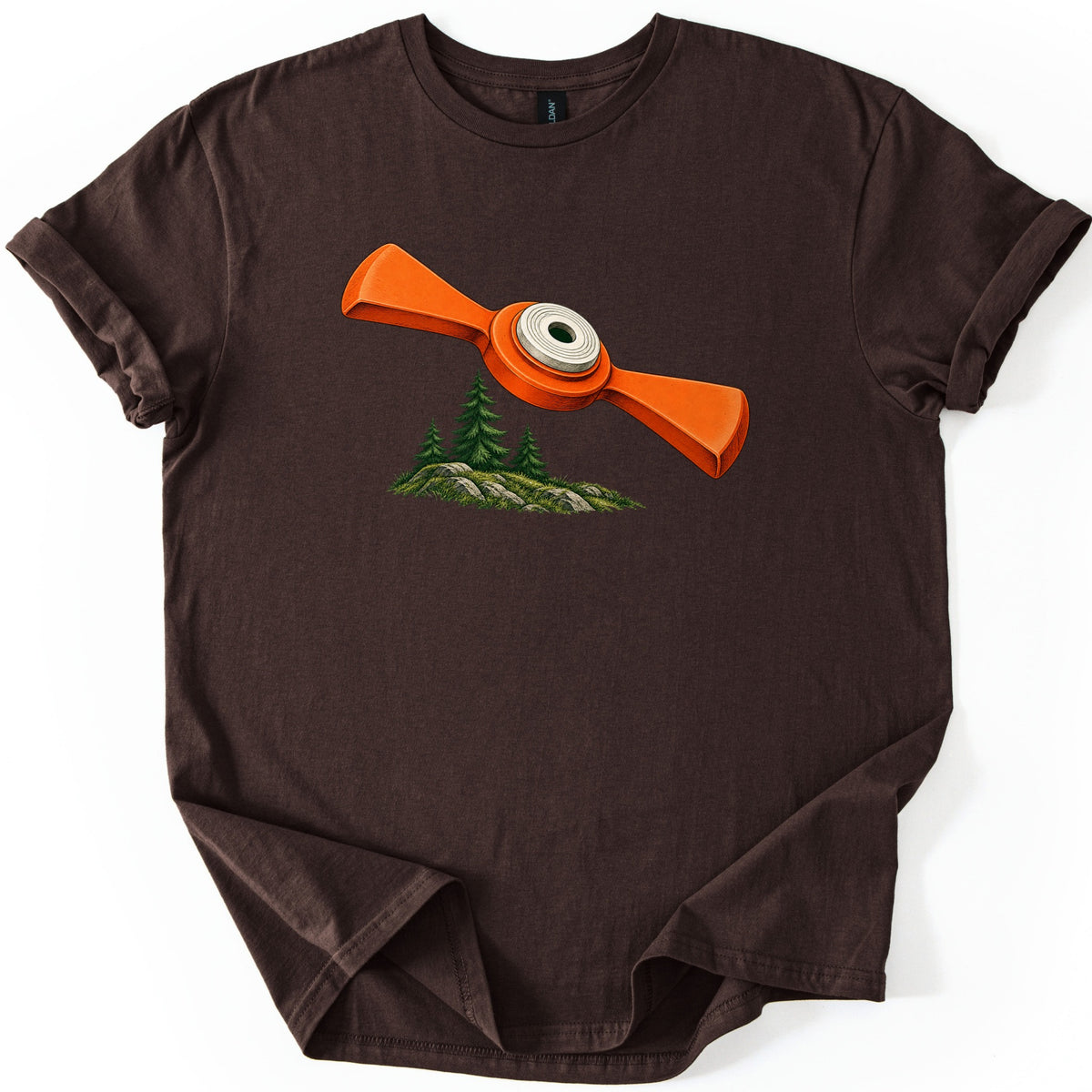 Winged Target Over the Pines Comfort Colors T-shirt in Dark Chocolate, laid flat. An orange clay target with two flared wings and a white center ring flies over a small mossy hill with three pine trees, with no text. The shirt lies flat on white with rolled sleeves.