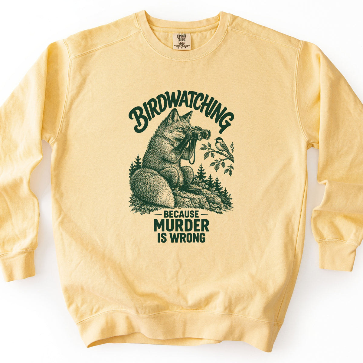 Birdwatching Because Murder Is Wrong Comfort Colors crewneck sweatshirt in Butter, laid flat. A dark green sketch of a fox on a rock using binoculars to watch a small bird on a leafy branch, with pine trees behind. Birdwatching arches above; Because Murder Is Wrong is below. White background.