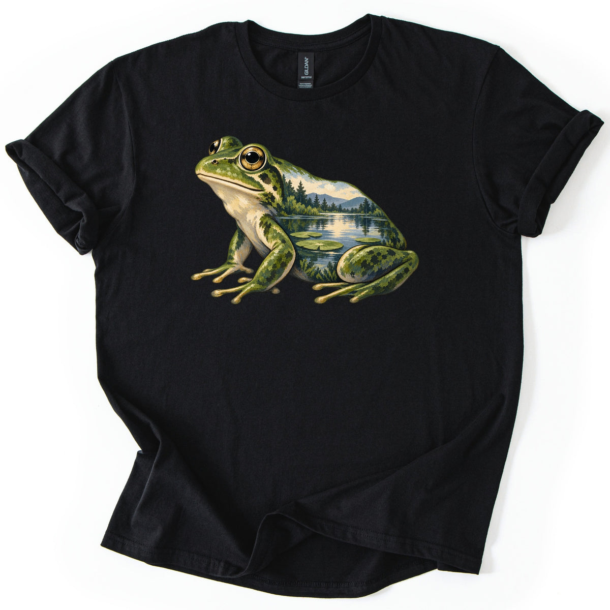 Lily Pond Frog Comfort Colors T-shirt in Black, laid flat. A painted green frog sits in profile, its body filled with a lake scene of pine trees, mountains and lily pads. No words are printed. The shirt has cuffed sleeves on a white background.