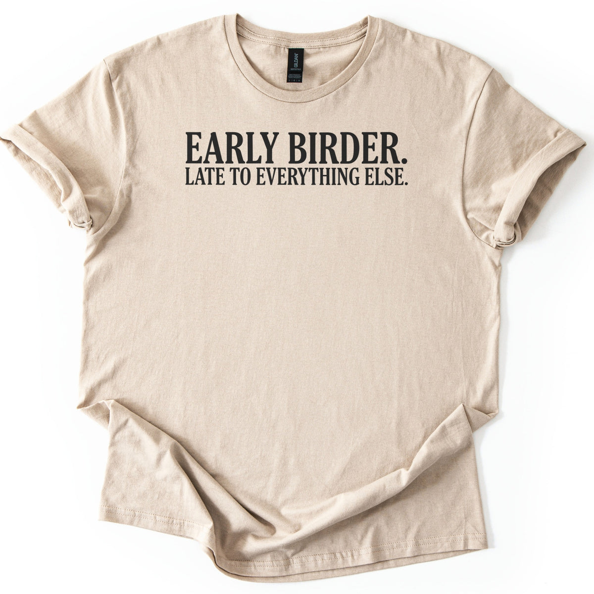 Early Birder Comfort Colors T-shirt in Sand, laid flat. Black serif capital letters across the chest read EARLY BIRDER. LATE TO EVERYTHING ELSE. The shirt lies on a white background with its short sleeves rolled up.
