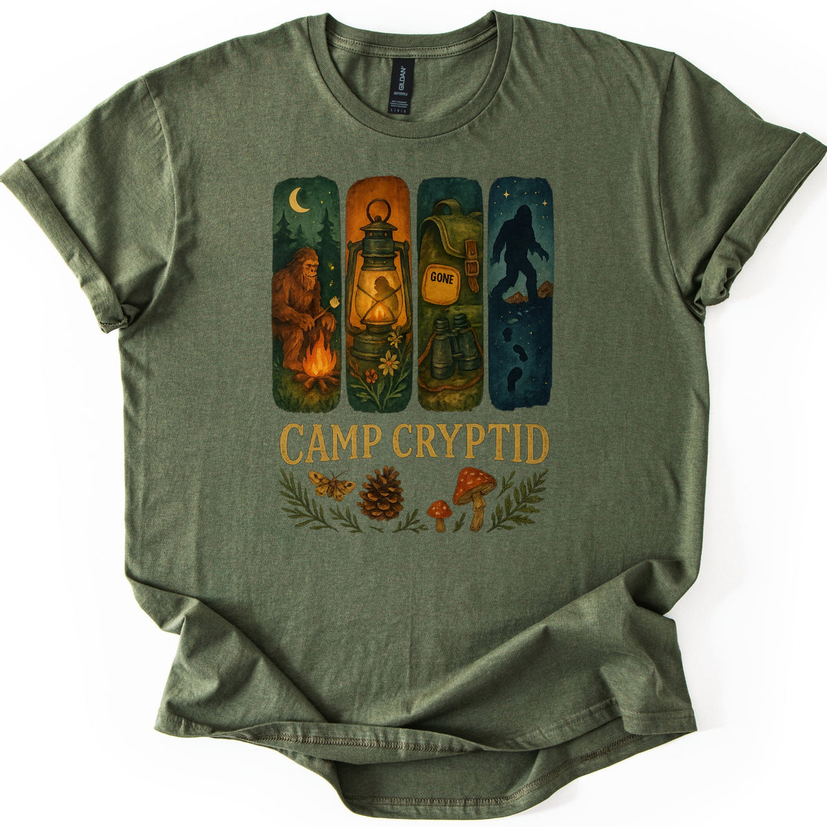 Camp Cryptid Big Foot Comfort Colors T-shirt in Military Green, laid flat. Four painted panels show Bigfoot at a campfire, a lit lantern, a backpack marked GONE, and Bigfoot's silhouette under stars, above the words Camp Cryptid and a moth, pinecone and mushrooms. Shown on a white background.