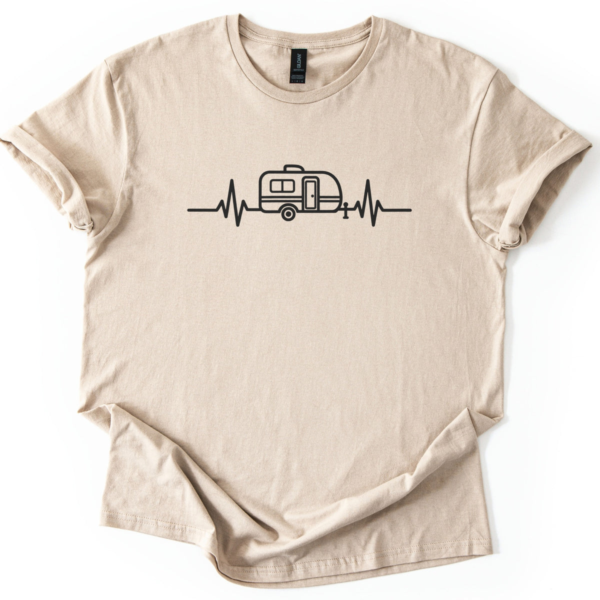 Camper Heartbeat Comfort Colors T-shirt in Sand, laid flat. A black line drawing of a small camper trailer with a window, door, wheel and hitch jack sits in the middle of a heartbeat line across the chest, with no words. The sleeves are cuffed on a white background.