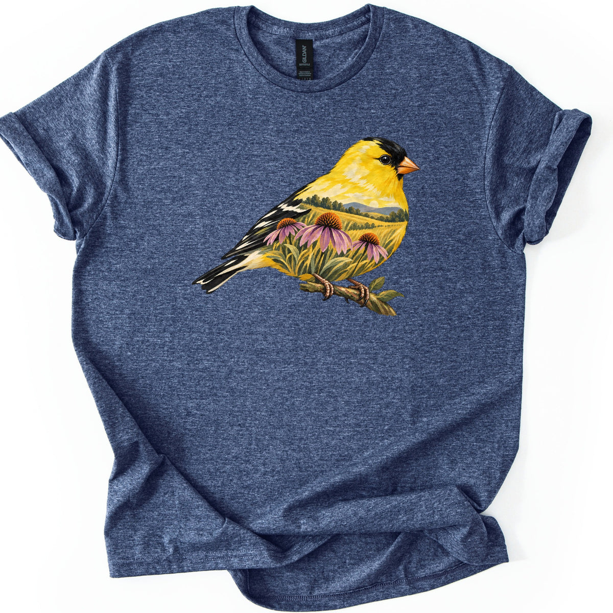 Goldfinch Meadow Comfort Colors T-shirt in Heather Navy, laid flat. A yellow goldfinch with a black cap perches on a leafy branch, its body filled with purple coneflowers, meadow grass and distant hills. No text is printed. The shirt lies on white with rolled sleeves.