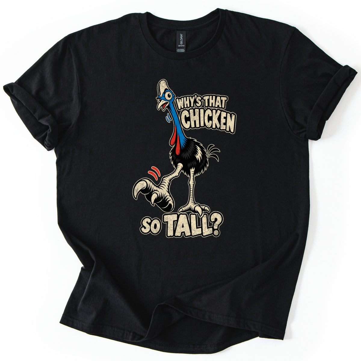 Why's That Chicken So Tall Comfort Colors T-shirt in Black, laid flat. A cartoon cassowary with a bony white crest, blue neck and red wattles raises a giant clawed foot beside the words Why's That Chicken So Tall? The shirt lies on a white surface with rolled sleeves.