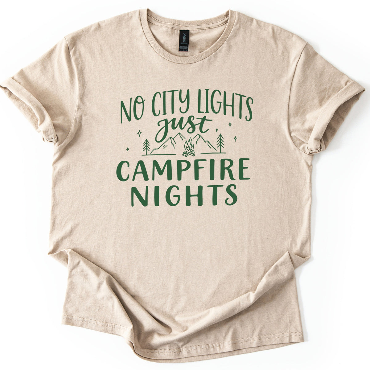 Campfire Nights Comfort Colors T-shirt in Sand, laid flat. Dark green print reads No City Lights just Campfire Nights, with a line drawing of mountains, pine trees, stars and a small campfire. The sleeves are rolled and the shirt lies on a white background.