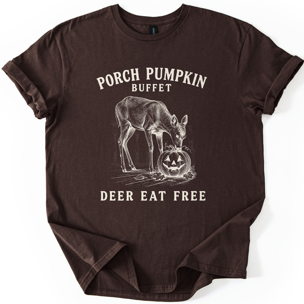 Porch Pumpkin Buffet Comfort Colors T-shirt in Dark Chocolate, laid flat. A cream engraving-style drawing of a deer nibbling a carved jack-o'-lantern on a porch with fallen leaves, between the words Porch Pumpkin Buffet and Deer Eat Free. Sleeves are rolled, on a white background.