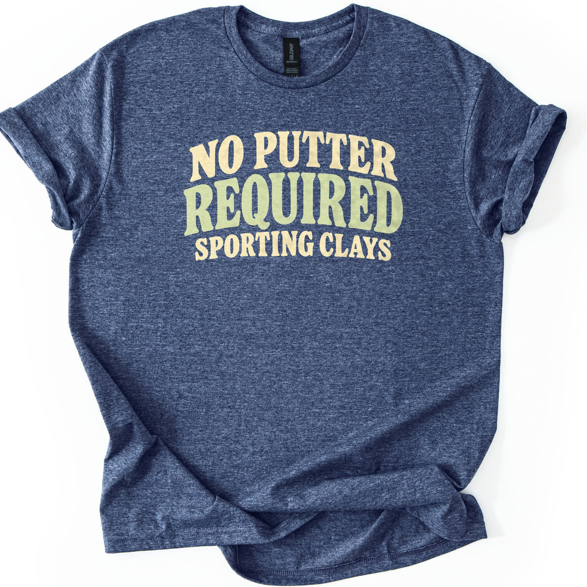 No Putter Required Comfort Colors T-shirt in Heather Navy, laid flat. Wavy retro letters read NO PUTTER in cream, REQUIRED in larger sage green, and SPORTING CLAYS in cream below. The heathered shirt lies on a white background with its sleeves rolled.