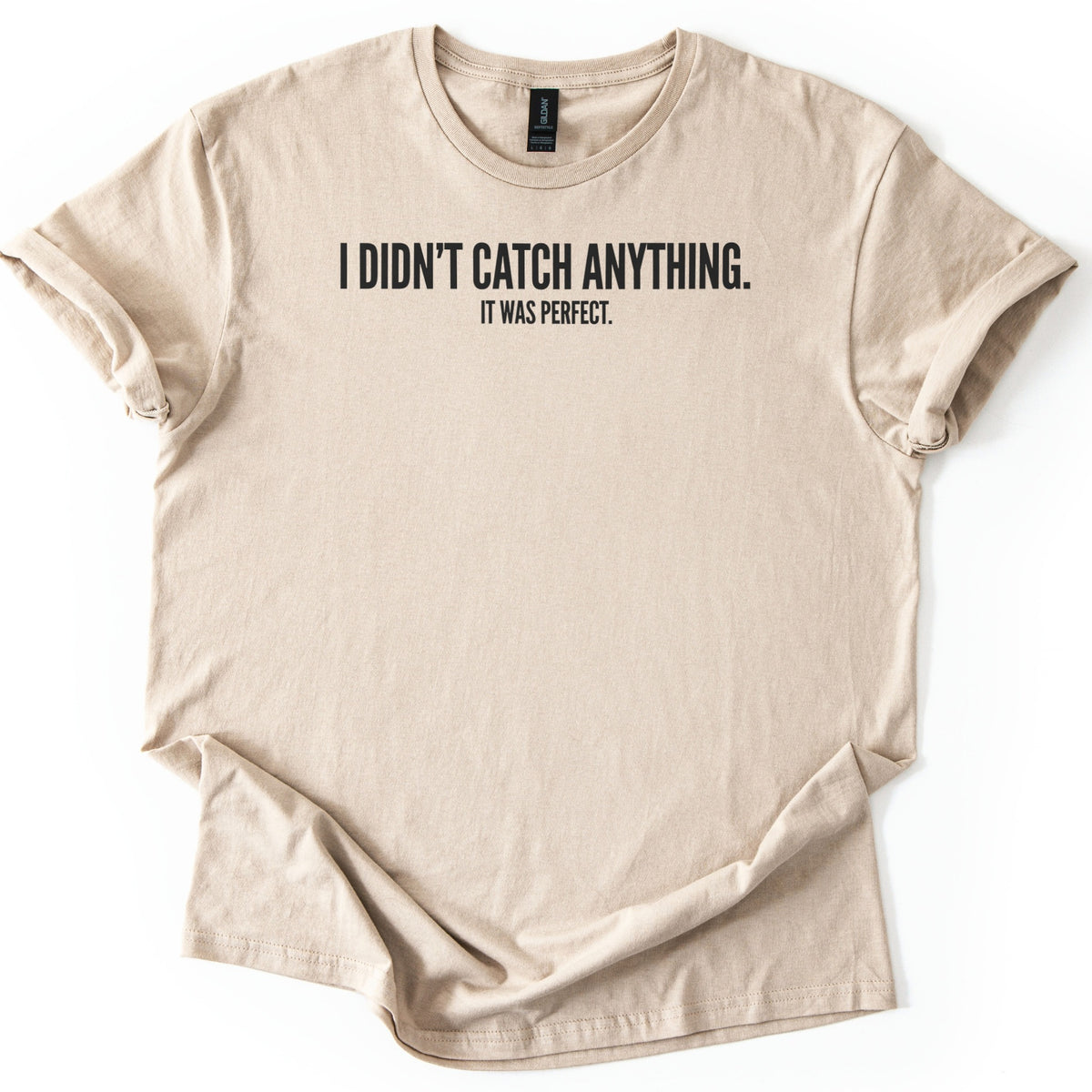 Didn't Catch Anything Comfort Colors T-shirt in Sand, laid flat. Black block letters across the chest read I DIDN'T CATCH ANYTHING. with smaller text below reading IT WAS PERFECT. The shirt has cuffed sleeves and lies on a white background.