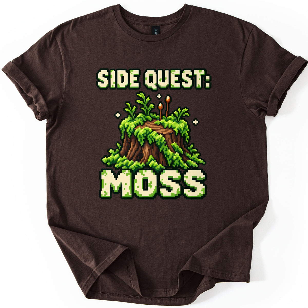Side Quest Moss Comfort Colors T-shirt in Dark Chocolate, laid flat. A pixel-art mossy tree stump with ferns, two little spore stalks and sparkles, framed by the words Side Quest: above and Moss below in green-speckled cream letters. Shown on a white background.