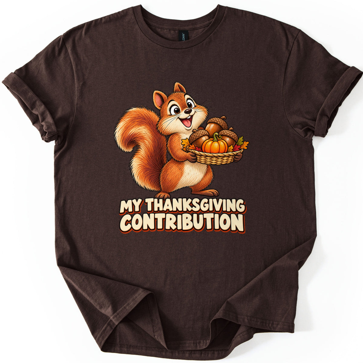 My Thanksgiving Contribution Comfort Colors T-shirt in Dark Chocolate, laid flat. A cheerful cartoon squirrel holds a basket of acorns, a small pumpkin and fall leaves above the words My Thanksgiving Contribution in cream letters outlined in orange. The shirt lies on a white surface with cuffed sleeves.