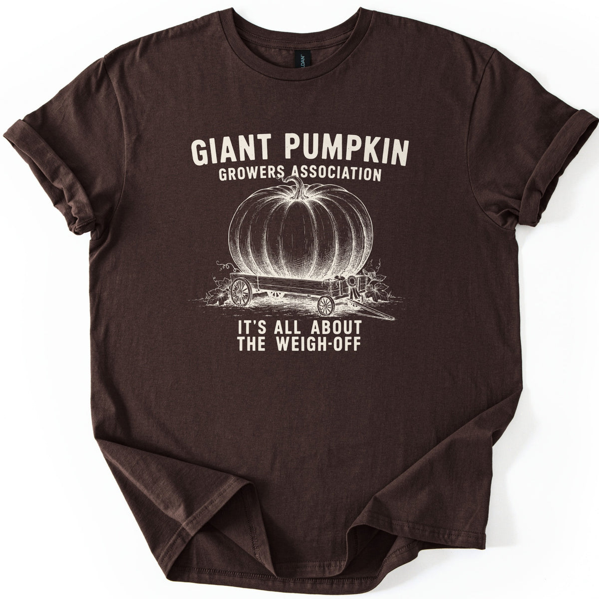 Giant Pumpkin Growers Association Comfort Colors T-shirt in Dark Chocolate, laid flat. A cream engraving-style drawing of a giant pumpkin on a wooden wagon with a prize ribbon sits between the words Giant Pumpkin Growers Association and It's All About the Weigh-Off. Sleeves cuffed, on white.