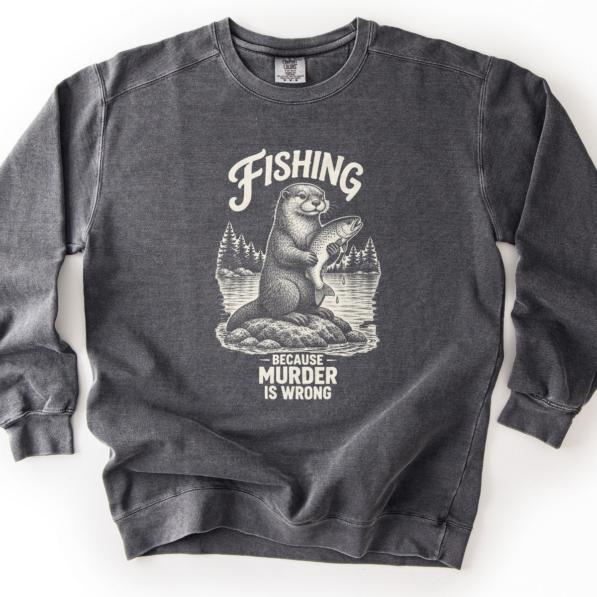Fishing Because Murder Is Wrong Comfort Colors crewneck sweatshirt in Pepper, laid flat. A cream etched otter perches on a lake rock clutching a dripping trout, with pine trees behind it. The word Fishing curves above it and Because Murder Is Wrong sits below. Laid on a white surface.