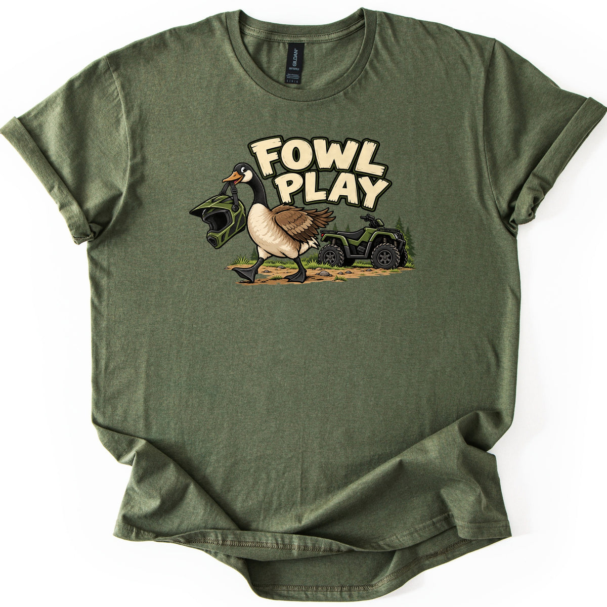 Fowl Play Comfort Colors T-shirt in Military Green, laid flat. A cartoon Canada goose carries a green motocross helmet in its beak past a green ATV and pine trees, below the words Fowl Play. The shirt lies on a white background with cuffed sleeves and a wavy hem.