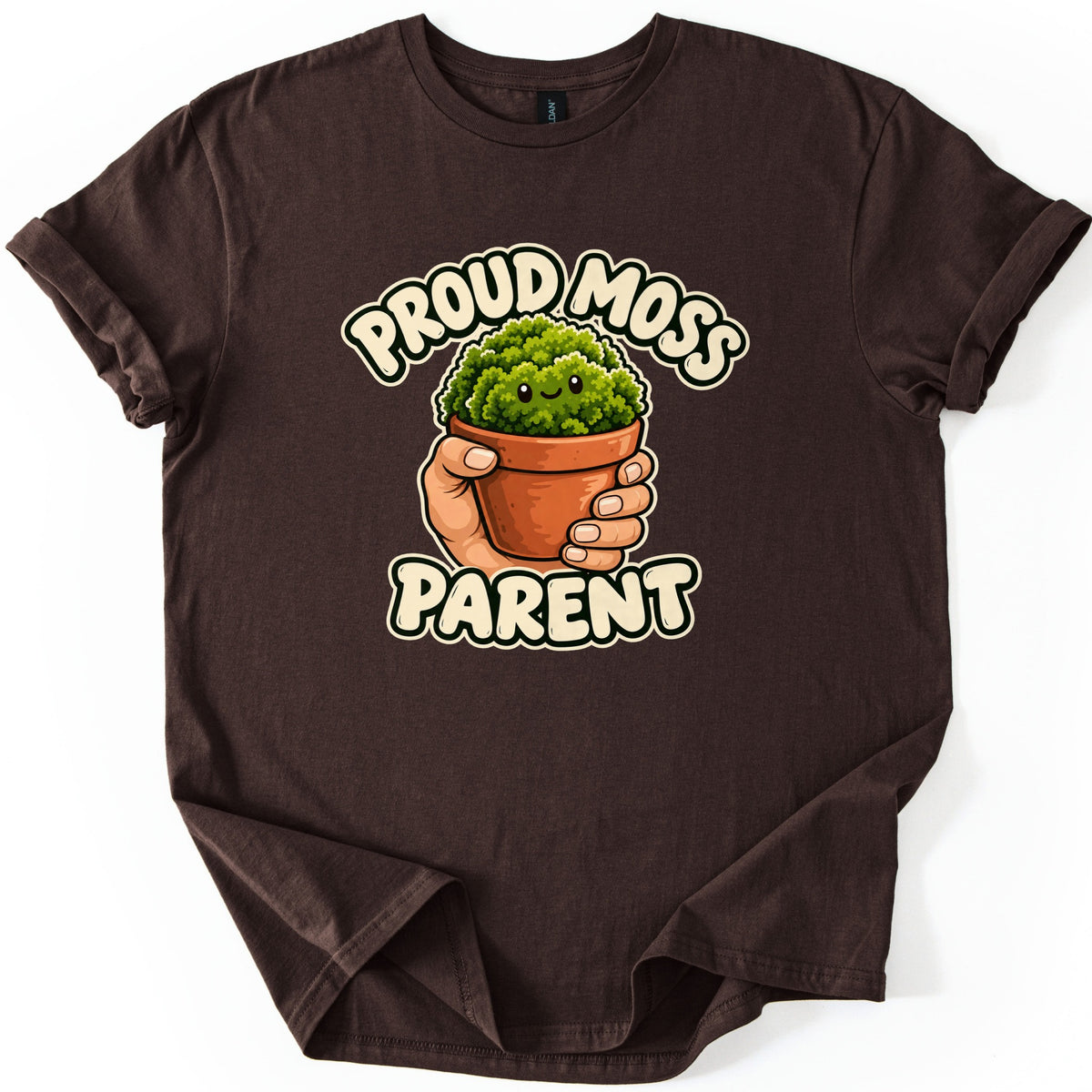 Proud Moss Parent Comfort Colors T-shirt in Dark Chocolate, laid flat. A cartoon hand holds a terracotta pot of smiling green moss between the words Proud Moss Parent in cream bubble letters. The shirt has cuffed sleeves and a slightly folded hem on a white background.