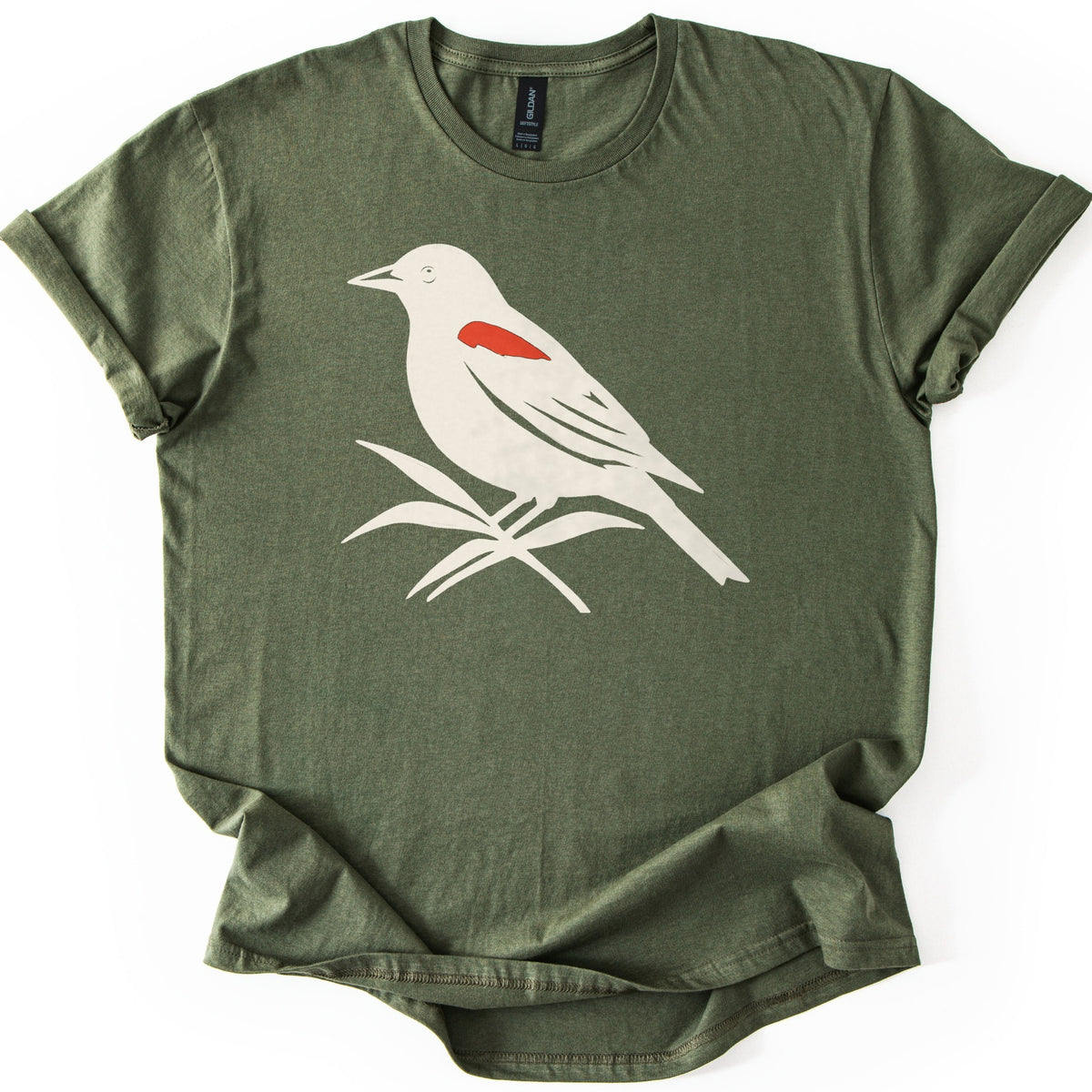 Red Winged Blackbird Comfort Colors T-shirt in Military Green, laid flat. A cream silhouette of a red-winged blackbird with a red shoulder patch, perched on slender leaves, with no words. The shirt has rolled sleeves and lies on a white background.
