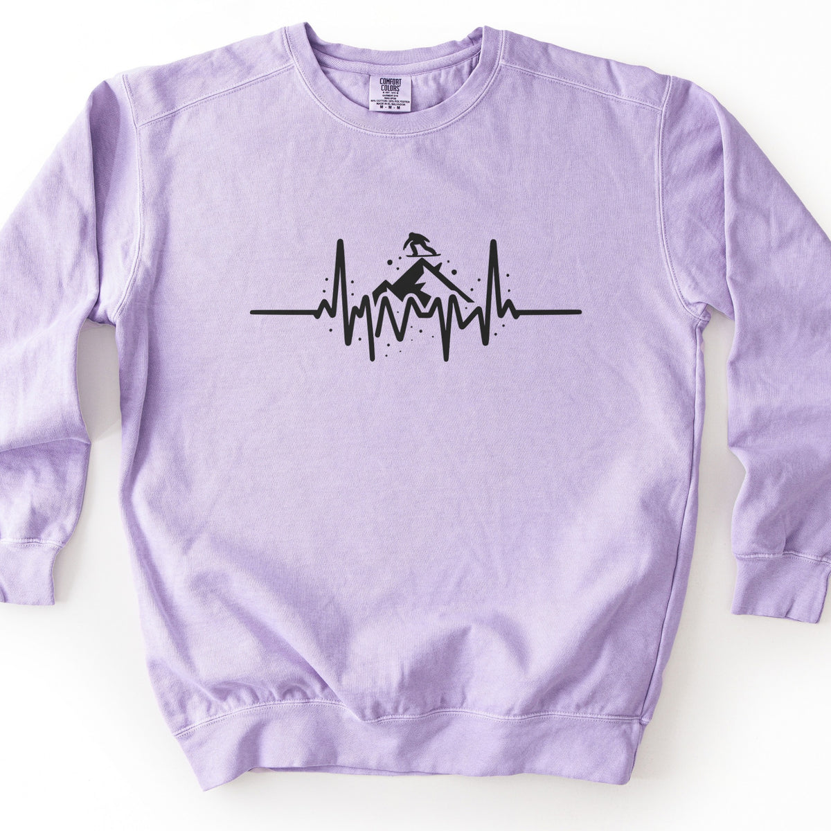 Snow Boarder Heartbeat Comfort Colors crewneck sweatshirt in Orchid, laid flat. A black heartbeat line runs across the chest, rising into a mountain peak with a snowboarder riding on top and small dots of snow around it. No words. The sweatshirt lies on a white surface.