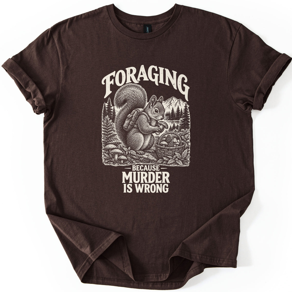 Foraging Murder Squirrel Comfort Colors T-shirt in Dark Chocolate, laid flat. Foraging arches over a cream etched squirrel wearing a backpack and holding a mushroom beside a basket of mushrooms, with pines and a mountain behind. Below: Because Murder Is Wrong. Cuffed sleeves, white background.