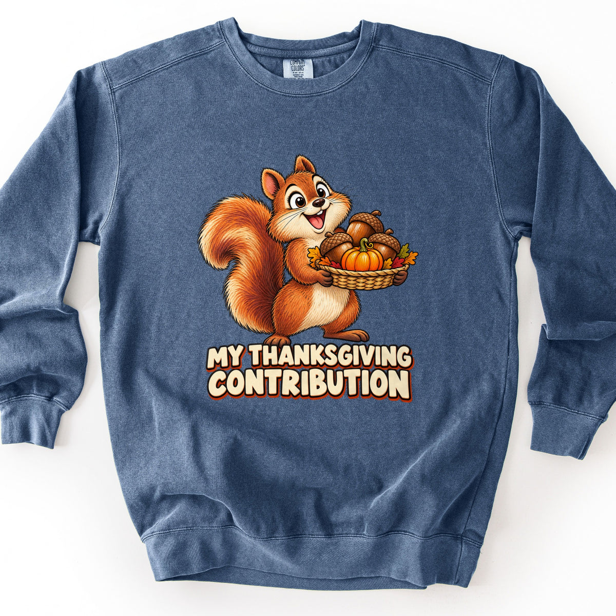 My Thanksgiving Contribution Comfort Colors crewneck sweatshirt in Denim, laid flat. A smiling cartoon squirrel holds a woven basket of acorns, a small pumpkin and autumn leaves above the words My Thanksgiving Contribution. The sweatshirt lies on a white surface.