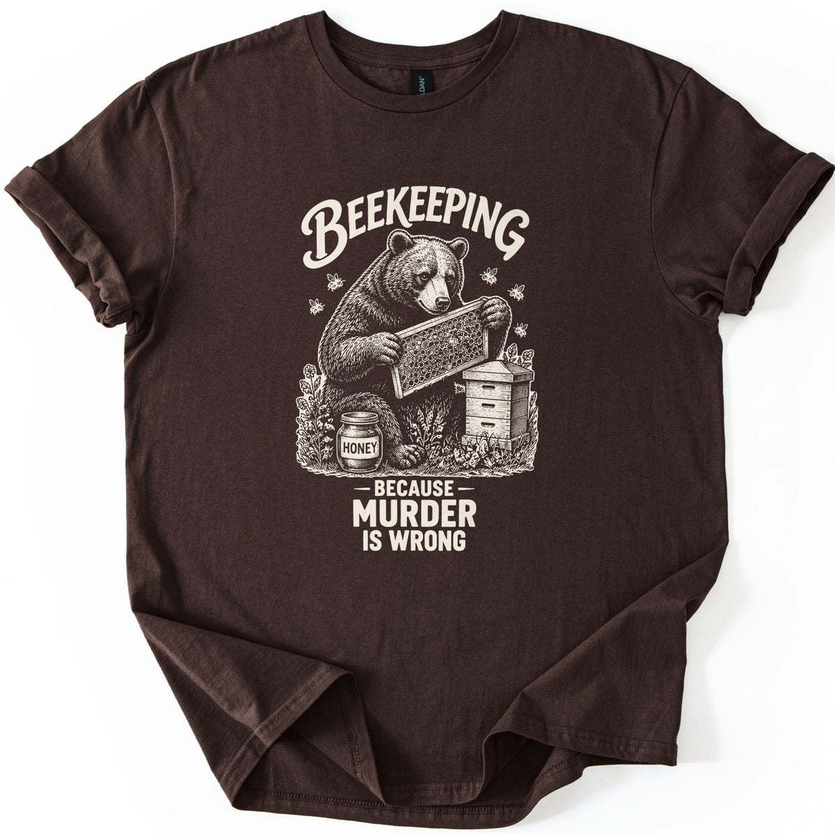 Beekeeping Murder Bear Comfort Colors T-shirt in Dark Chocolate, laid flat. A cream etched drawing of a bear holding a honeycomb frame by a beehive and a jar labeled Honey, with bees flying, under the word Beekeeping and above Because Murder Is Wrong. Shown on white with cuffed sleeves.