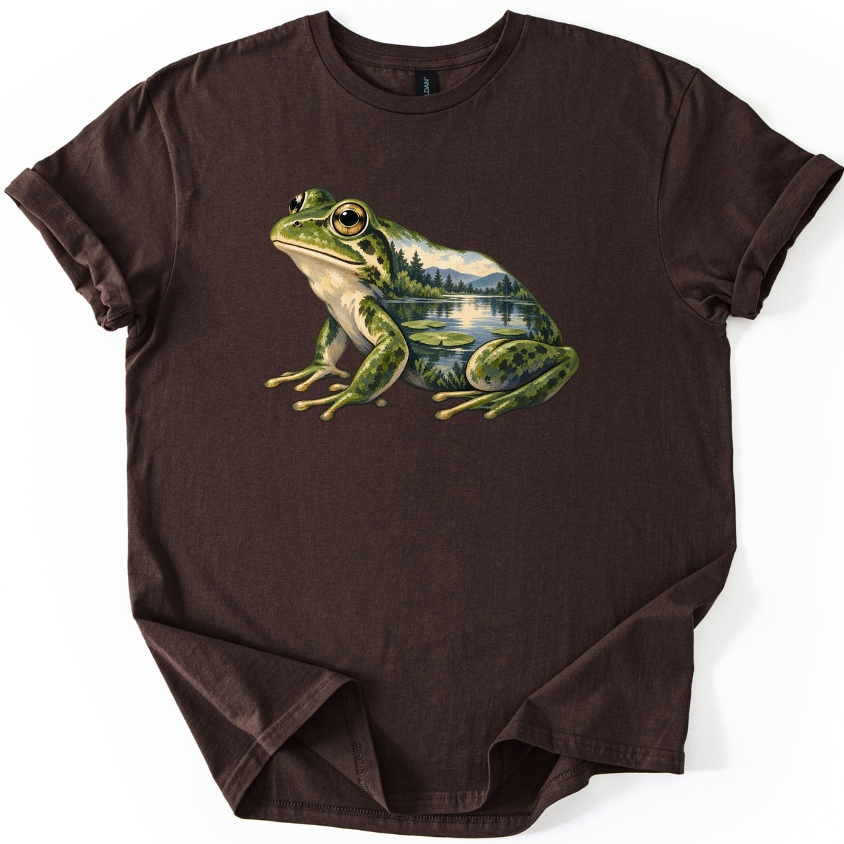 Lily Pond Frog Comfort Colors T-shirt in Dark Chocolate, laid flat. A painted green frog sits in profile, its body filled with a lake scene of pine trees, mountains and lily pads. No words are printed. The shirt has cuffed sleeves on a white background.