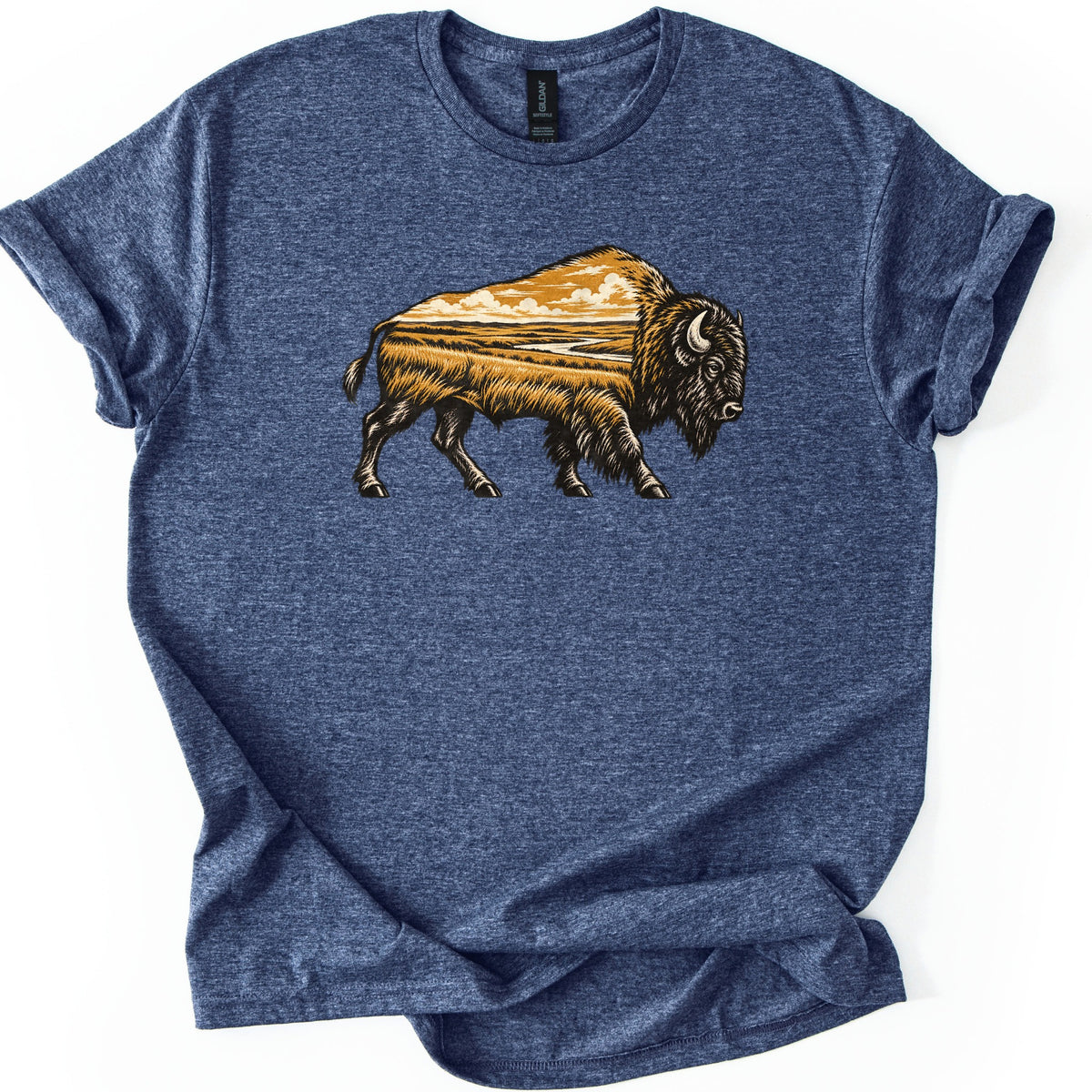 Prairie Bison Comfort Colors T-shirt in Heather Navy, laid flat. A woodcut-style bison walks in side profile, its body filled with a golden prairie scene of tall grass, a winding river and clouds. No words. The shirt has cuffed sleeves on a white background.