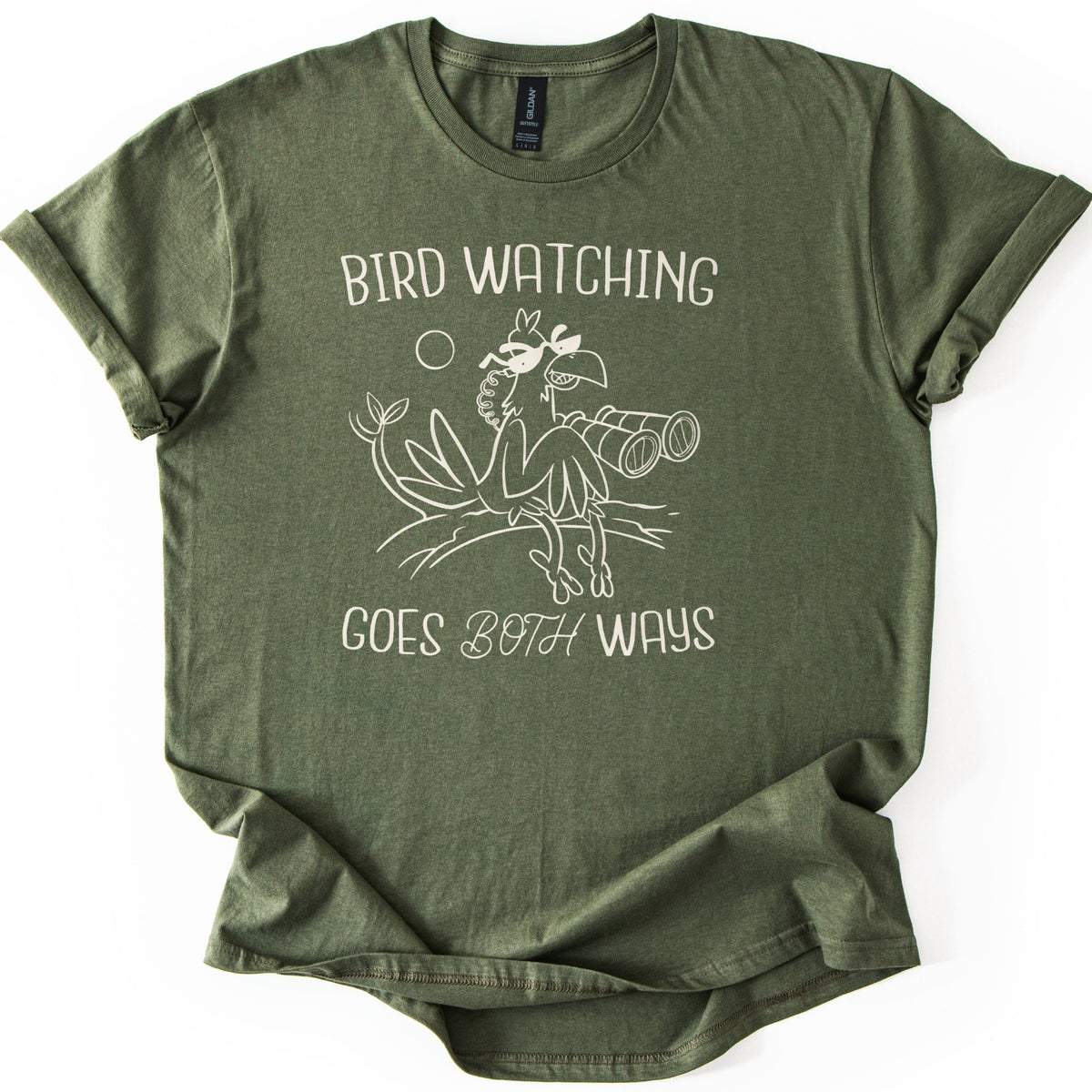 Birds Watch Back Birder Comfort Colors T-shirt in Military Green, laid flat. Cream line art of a cartoon bird in sunglasses perched on a branch beside a pair of binoculars, with a small sun, between the words Bird Watching Goes Both Ways. Sleeves rolled, on a white background.