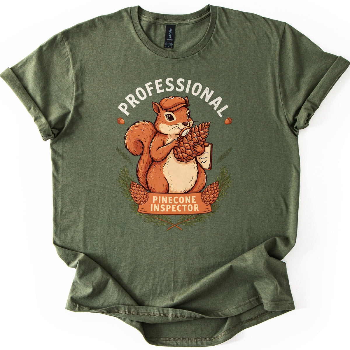 Professional Pinecone Inspector Comfort Colors T-shirt in Military Green, laid flat. A squirrel in a cap inspects a pinecone with a magnifying glass under the arched word Professional in white, above a banner reading Pinecone Inspector framed by pine branches. Sleeves are cuffed on a white surface.