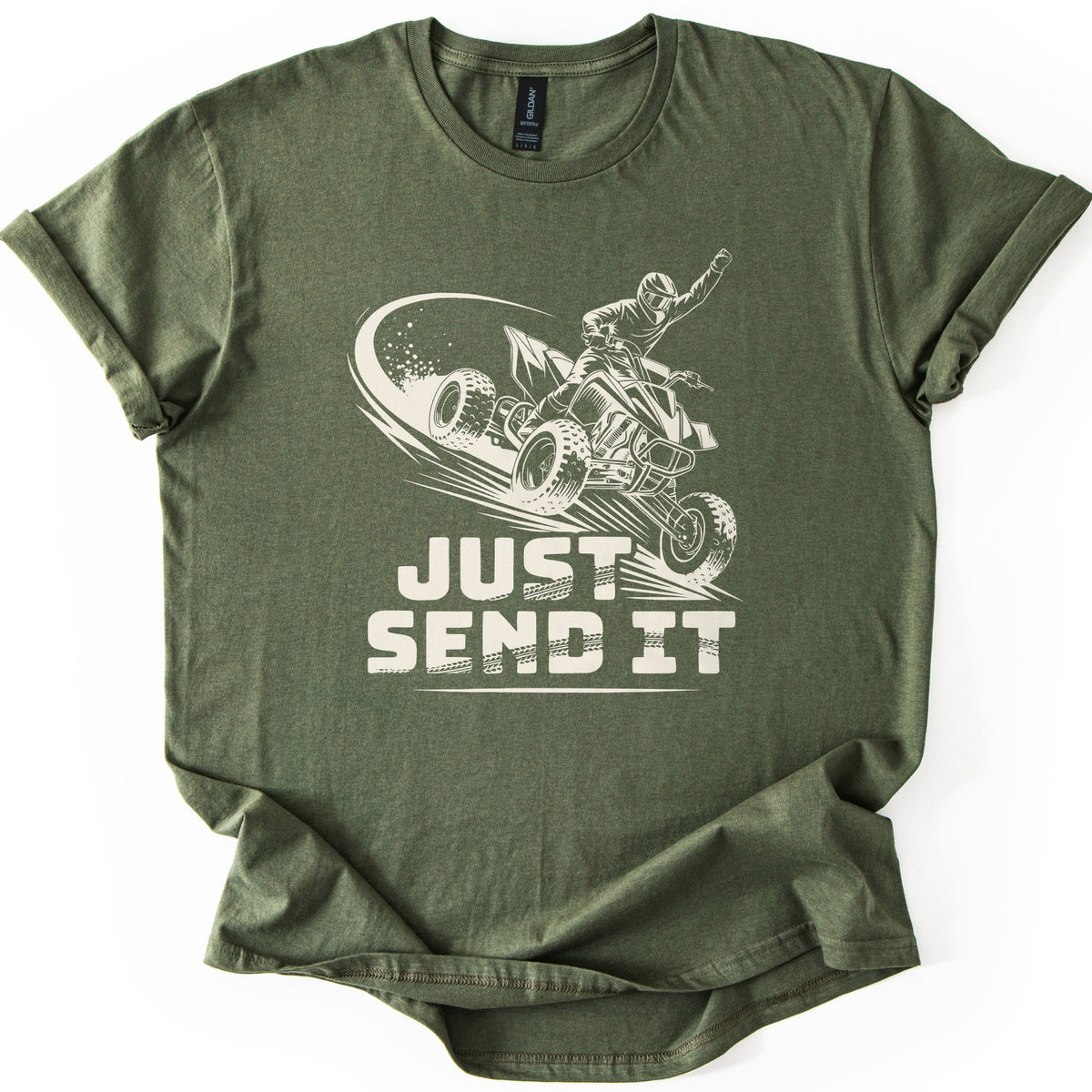 ATV Just Send It Comfort Colors T-shirt in Military Green, laid flat. A cream drawing of a helmeted rider jumping a quad ATV with a raised fist and a dust trail, above the words Just Send It in tire-tread lettering. The shirt has cuffed sleeves on a white surface.