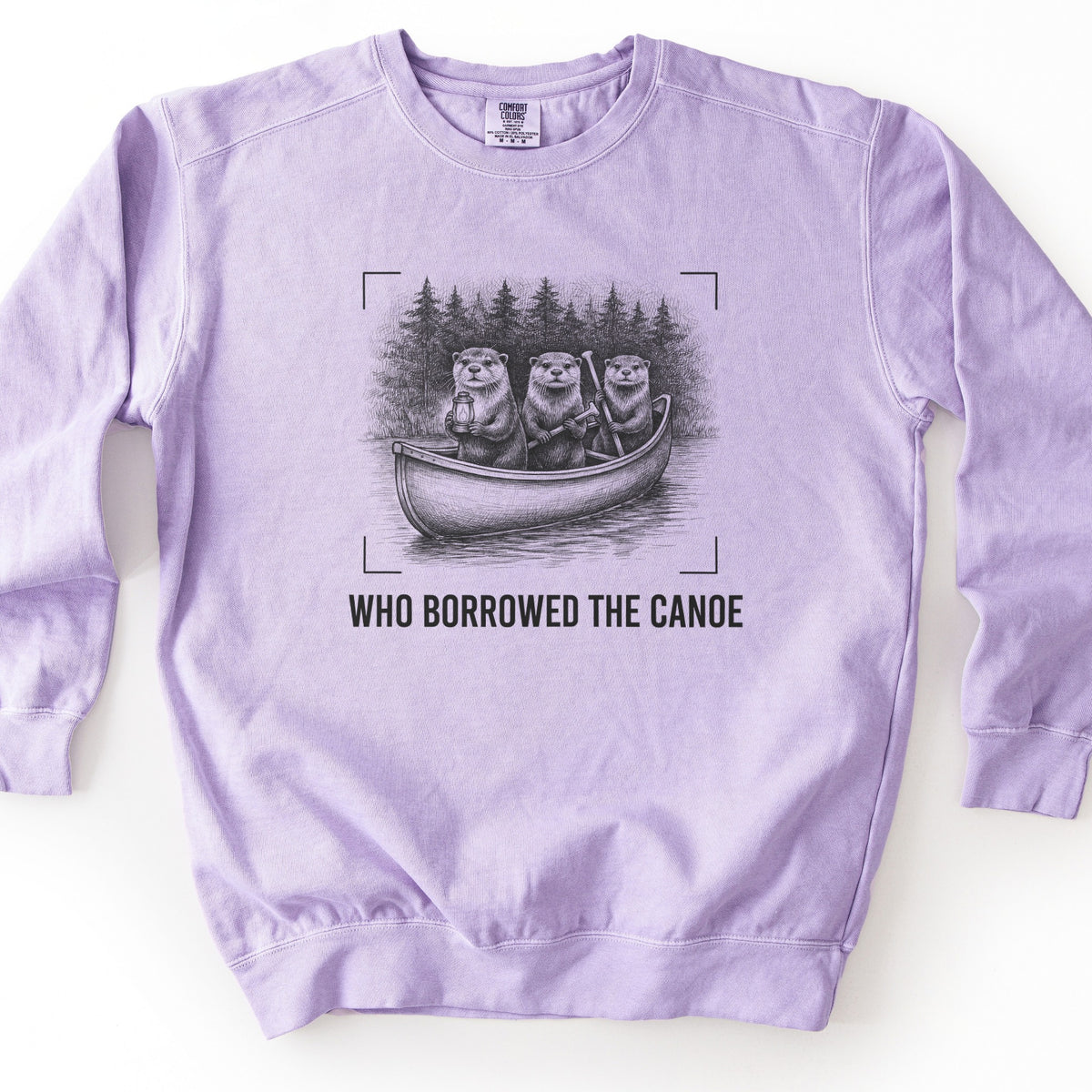 Who Borrowed The Canoe Comfort Colors crewneck sweatshirt in Orchid, laid flat. A black and gray sketch of three otters in a canoe on a lake, one with a lantern and two with paddles, pine trees behind, framed by corner brackets, above the words WHO BORROWED THE CANOE. On a white surface.