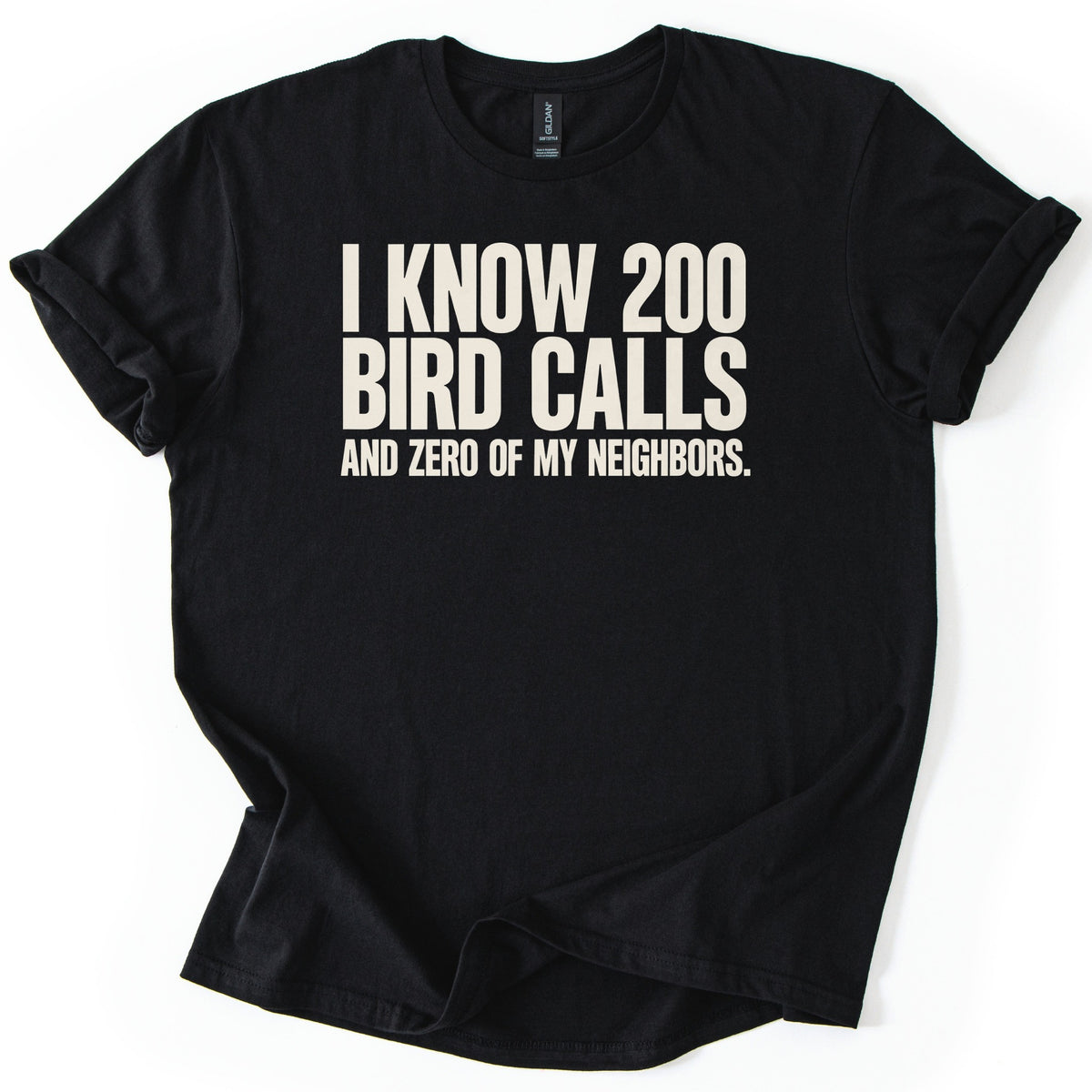 I Know 200 Bird Calls and Zero of My Neighbors Comfort Colors T-shirt in Black, laid flat. Bold cream capital letters across the chest read I Know 200 Bird Calls and Zero of My Neighbors. The shirt lies on a white background with rolled sleeves and a loosely rumpled hem.