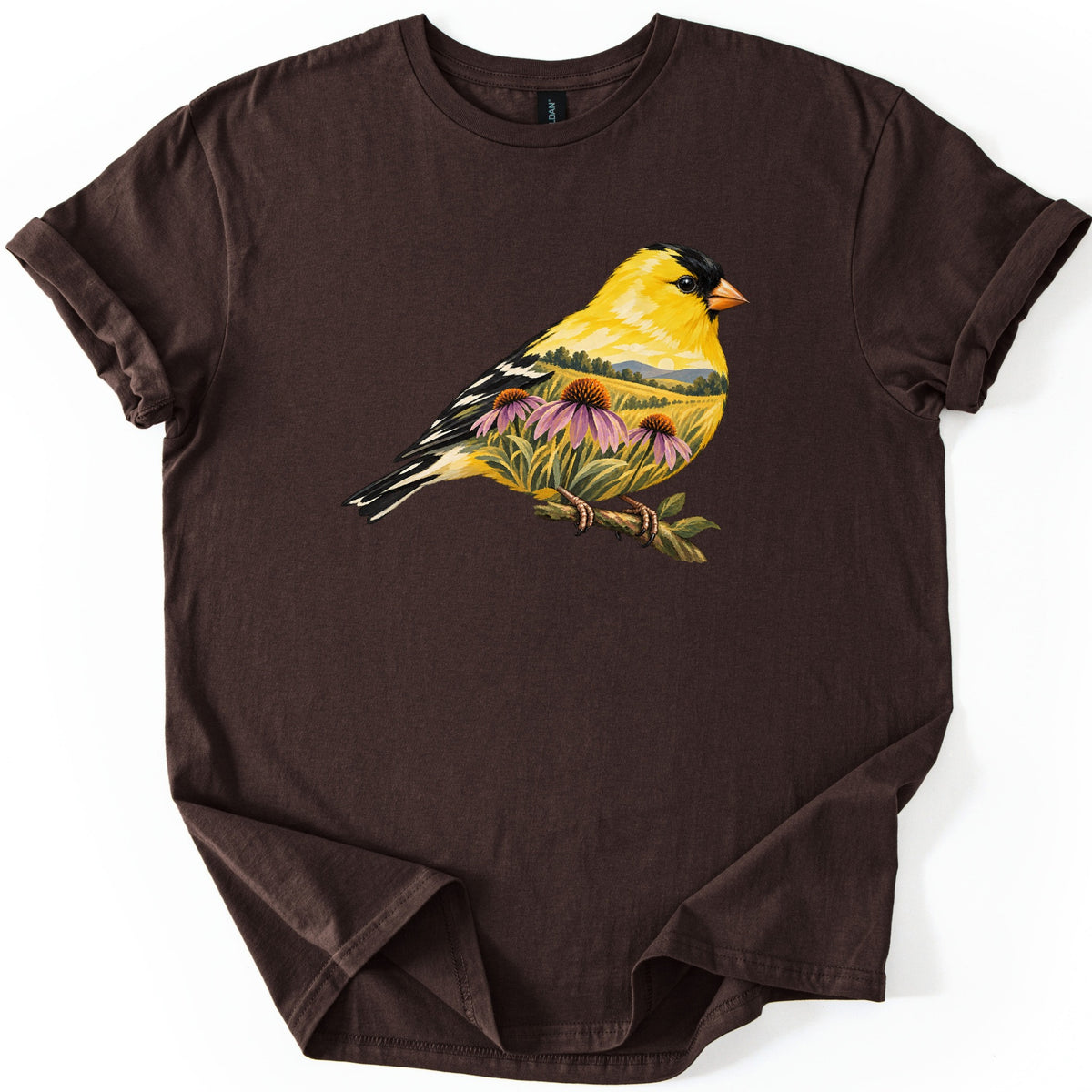 Goldfinch Meadow Comfort Colors T-shirt in Dark Chocolate, laid flat. A painted goldfinch with black cap and wings sits on a branch, its yellow body blending into a meadow of pink coneflowers, grass and hills. No words. Sleeves rolled, laid on a white background.