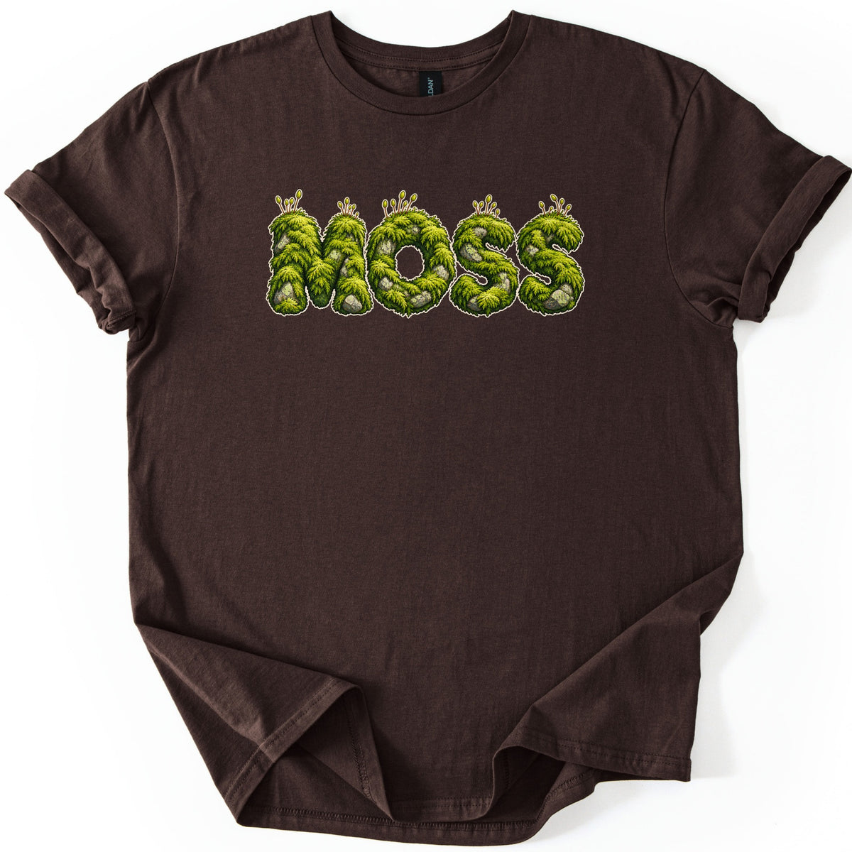 Moss Comfort Colors T-shirt in Dark Chocolate, laid flat. The word MOSS is printed across the chest in green moss-covered letters with gray stones, small sprouting stalks, and a thin light outline. The shirt has rolled sleeves and lies on a white background.