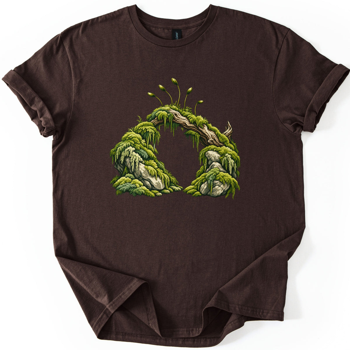 Moss Arch Comfort Colors T-shirt in Dark Chocolate, laid flat. A moss-covered fallen log spans two mossy boulders to form an arch, topped by slender spore stalks. No words are printed. The sleeves are cuffed and the shirt rests on a white background.