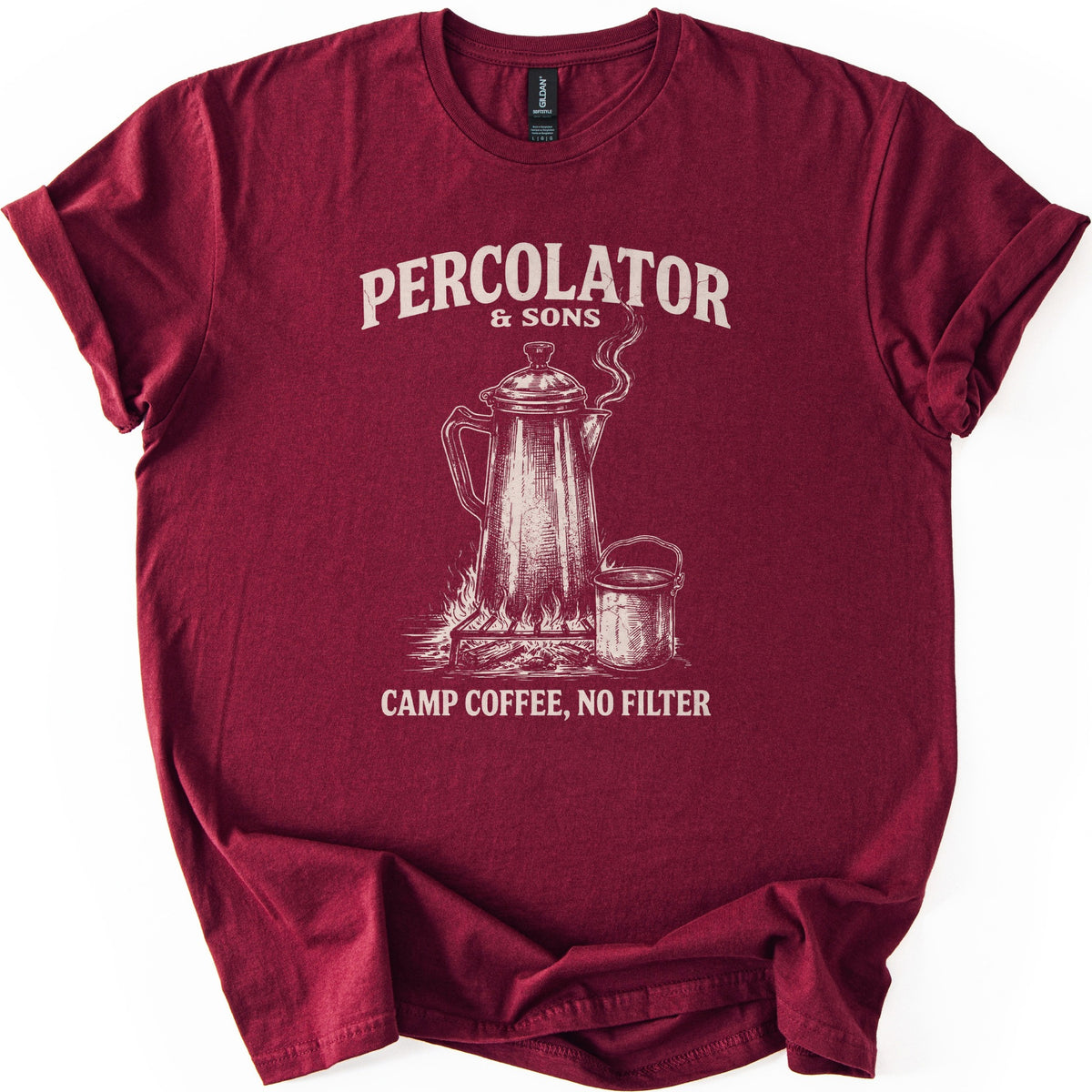 Percolator & Sons Comfort Colors T-shirt in Maroon, laid flat. A sketched coffee percolator steams on a grate over a campfire beside a tin cup, under the words Percolator & Sons and above Camp Coffee, No Filter, in cream ink. The sleeves are rolled on a white background.