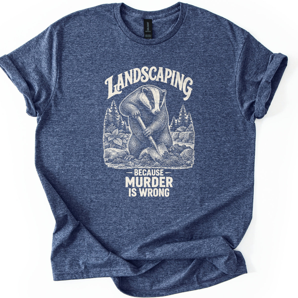 Landscaping Murder Badger Comfort Colors T-shirt in Heather Navy, laid flat. A cream engraving-style badger digs with a shovel among pine trees and rocks, under the arched word Landscaping and above Because Murder Is Wrong. Cuffed sleeves on a white background.